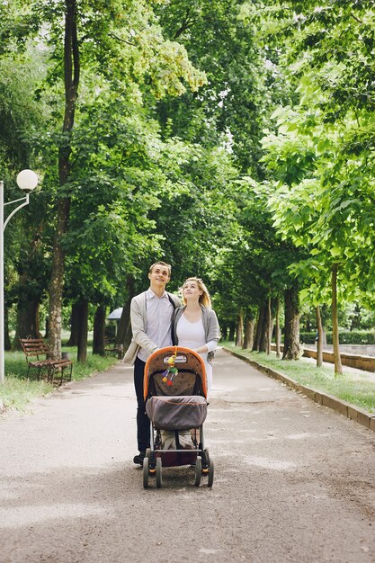 Pai e mãe jovem andando com seu bebê pelo parque em um carrinho