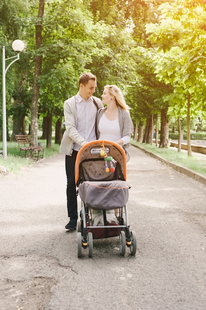 Pai e mãe jovem andando com seu bebê pelo parque em um carrinho