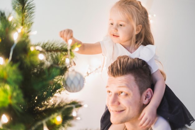 Pai feliz ao lado de árvore de Natal iluminada com filha