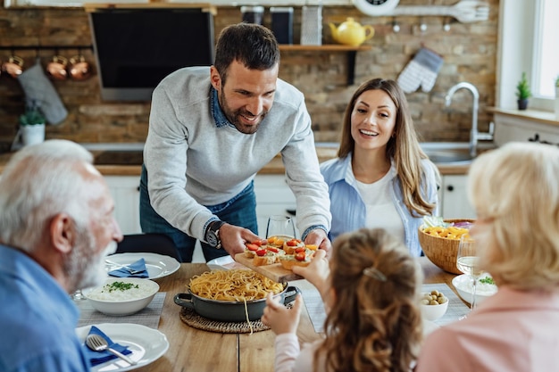 Pai feliz oferecendo bruschetta para sua filha enquanto almoça em família na mesa de jantar