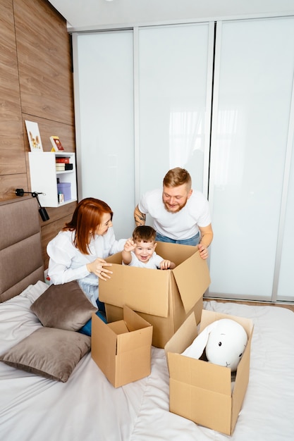 Pai, mãe e filho brincam no quarto com caixas de papel