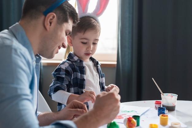 Pai mostrando seu filho como pintar ovos de Páscoa