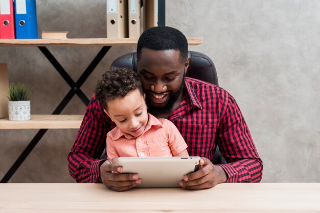 Pai negro e filho usando tablet na mesa