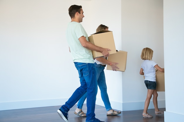 Pai segurando uma caixa de papelão e indo para o corredor atrás de esposa e filha