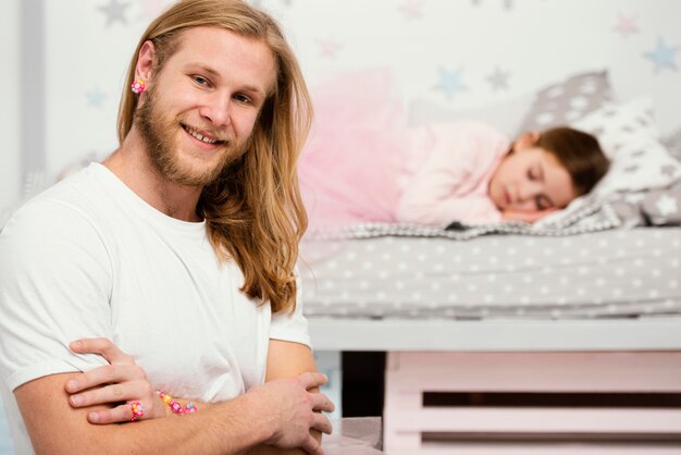 Pai sorridente posando ao lado da filha sonolenta em casa