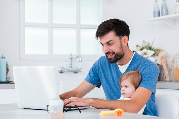 Pai trabalhando no laptop, segurando o bebê