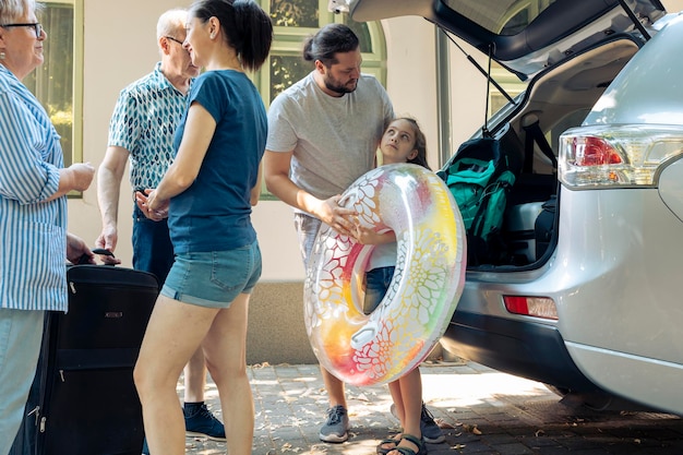 Pais com criança carregando malas no porta-malas, colocando bagagem no carro para sair em viagem de férias. Grande família com avós viajando em viagem de verão à beira-mar com inflável para lazer.