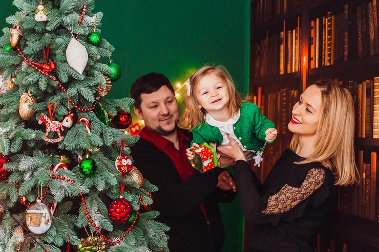 Foto grátis pais com pequena garota loira posam antes de uma árvore de natal na sala