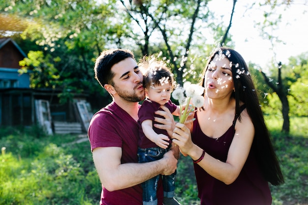 Pais com um bebê em seus braços, soprando dandelions