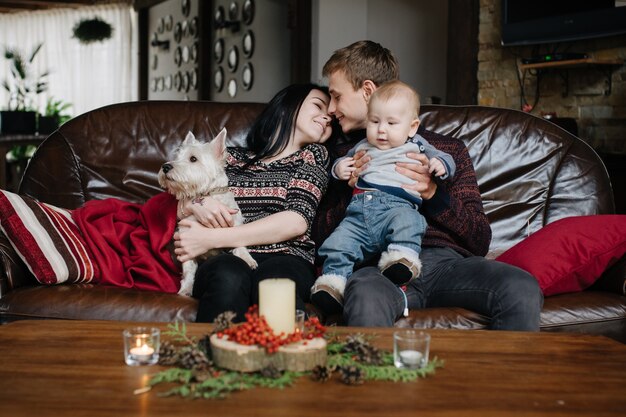 Pais com um bebê no Natal e um cão sentado no sofá