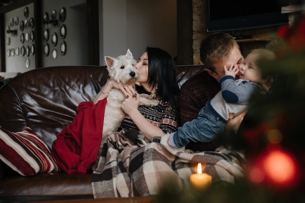 Pais com um bebê no Natal e um cão sentado no sofá