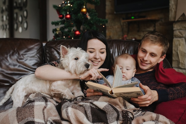 Pais com um bebê no Natal e um cão sentado no sofá