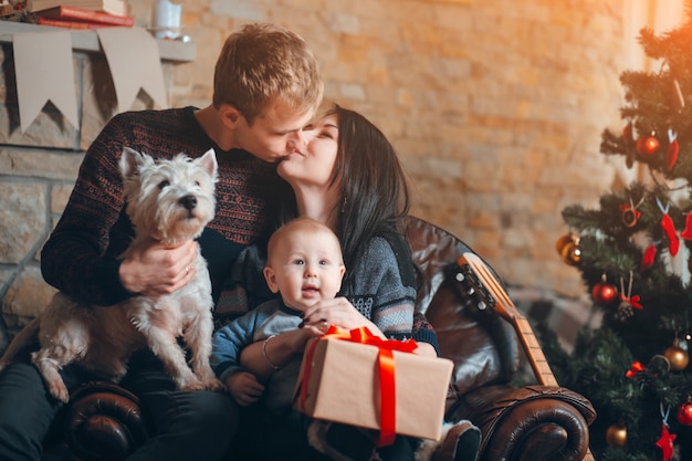 Pais com um cão e um bebê com um fundo da árvore de Natal