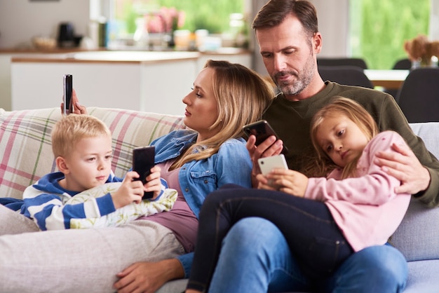 Pais e filhos usando celular na sala de estar