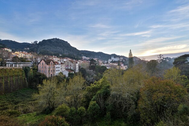 Paisagem de colinas cobertas de edifícios e florestas sob um céu nublado durante o pôr do sol