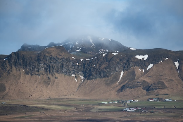 Paisagem de montanhas cobertas de neve e grama sob um céu nublado na Islândia