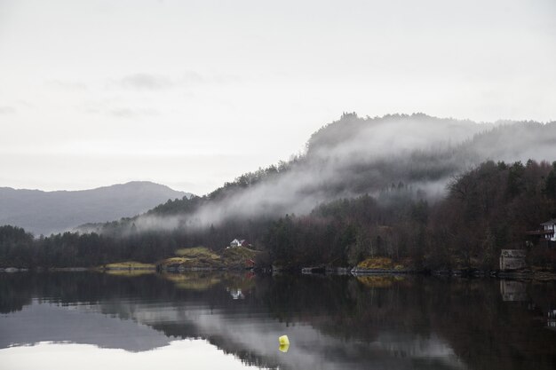 Paisagem de um lago cercado por montanhas cobertas de florestas e neblina, refletindo na água
