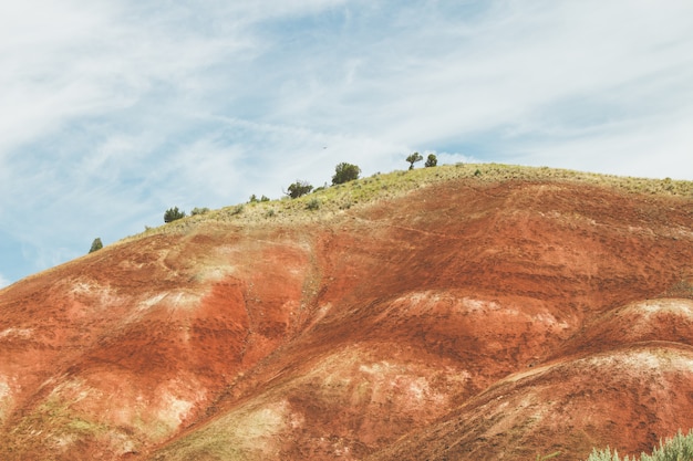 Paisagem de uma colina coberta de areia vermelha e vegetação sob um céu azul nublado