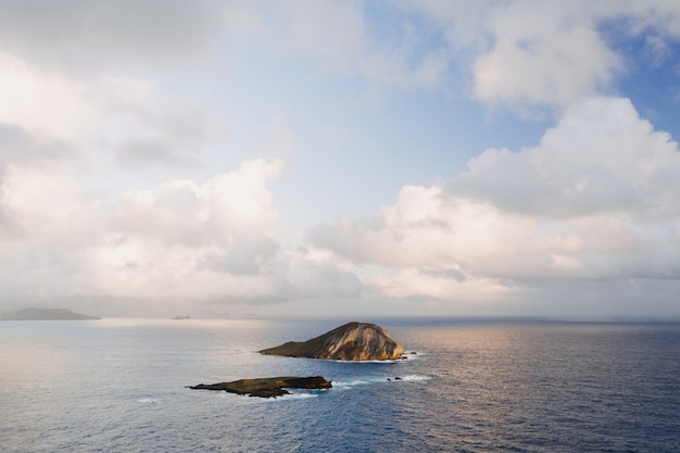 Paisagem de uma pequena ilha rodeada pelo mar sob um céu nublado e luz do sol