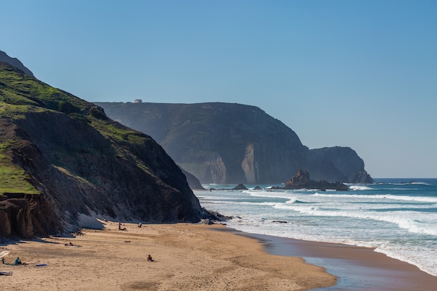 Paisagem de uma praia rodeada de mar e montanhas com pessoas ao redor em Portugal, Algarve