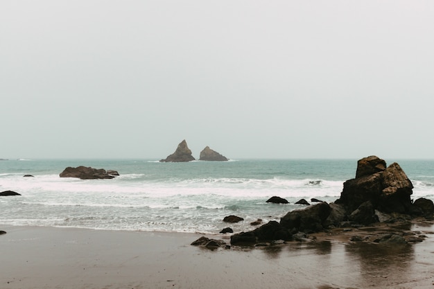 Paisagem do mar cercada por rochas e praia sob um céu nublado durante o dia