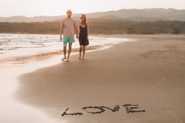 palavra amor na costa de areia e turva casal apaixonado no fundo andando