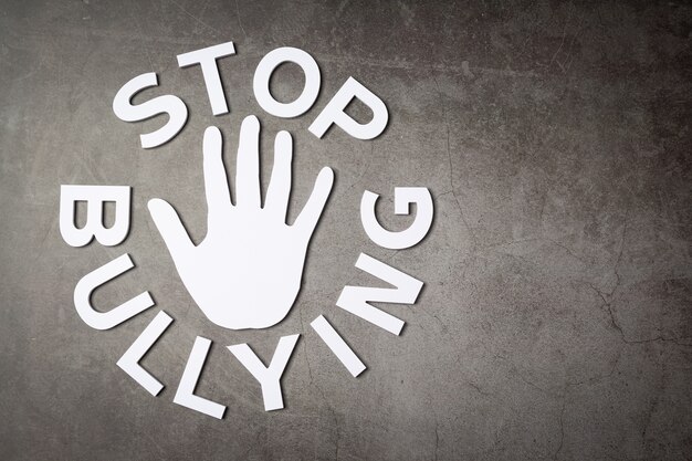 Palavra "pare de bullying" com sinal de mão na parede escura