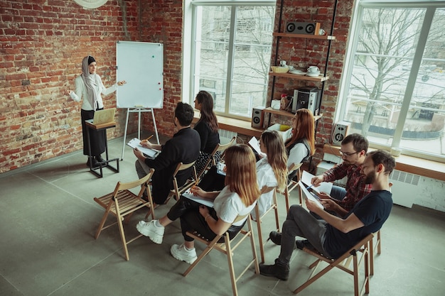 Foto grátis palestrante muçulmano feminino fazendo apresentação no corredor do workshop. audiência ou salão. visão de alto ângulo dos participantes na audiência.