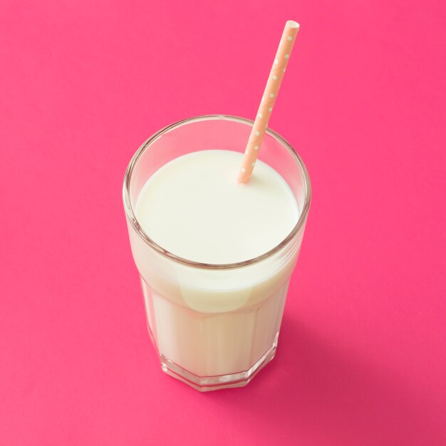 Palha bebendo no copo de leite sobre o pano de fundo-de-rosa