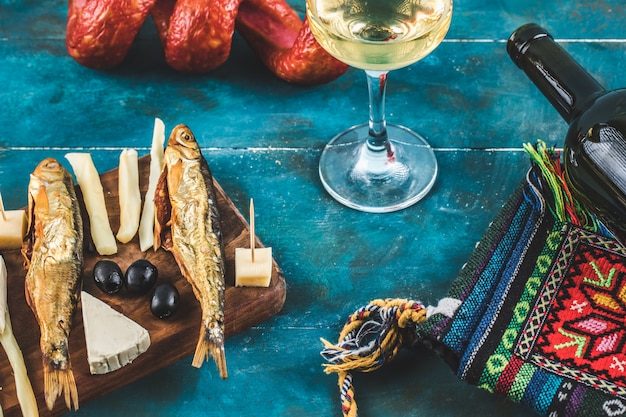 Palitos de queijo com peixe defumado em fundo azul com um copo de vinho