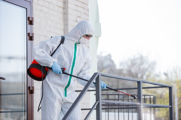 Foto grátis pandemia de coronavírus. um desinfetante em traje de proteção e máscara pulveriza desinfetantes na sala.
