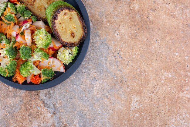 Panela de servir com rodelas de abobrinha frita e salada mista de vegetais em superfície de mármore