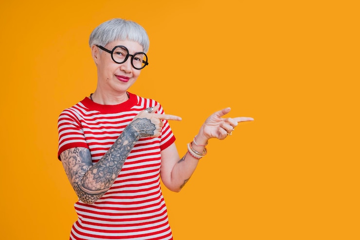 Foto grátis pano em forma de cabelo grisalho feminino asiático sênior com tatuagem braço em pé gesto com expressão confiante positiva mulher asiática antiga veste camiseta vermelha estilo de vida despreocupado felicidade idade de pensão