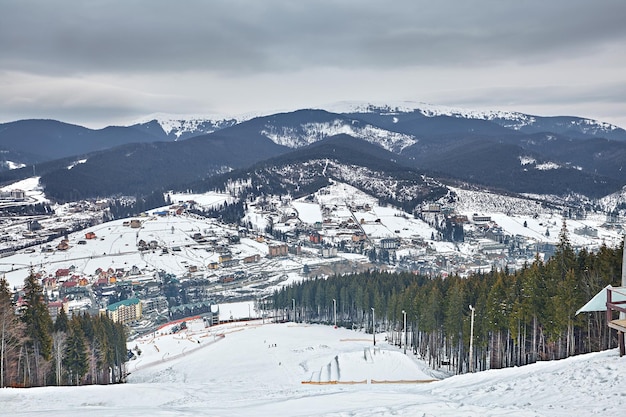 Panorama da estância de esqui, encosta, pessoas no teleférico, esquiadores na pista entre pinheiros verdes e lanças de neve. Copiar espaço