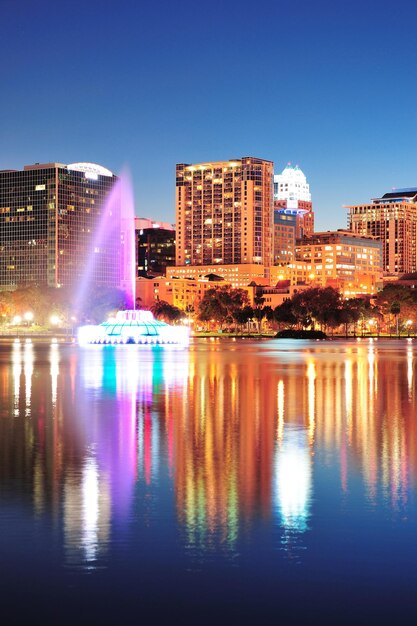 Panorama do horizonte do centro de Orlando sobre o Lago Eola à noite com arranha-céus urbanos, fonte e céu claro.