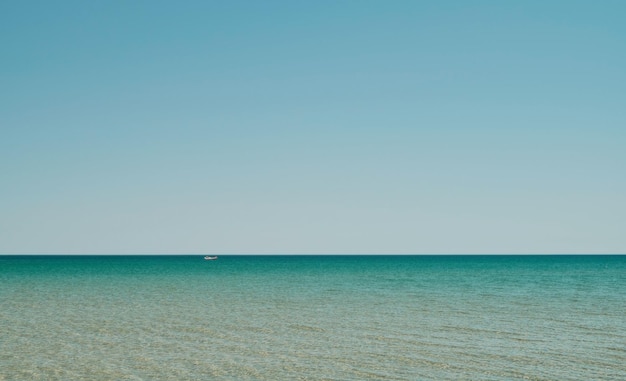 Foto grátis panorama do mar em águas rasas com reflexo do sol na água vasto mar aberto com ondas de ondulação de céu claro e mar calmo com bela luz solar barco vermelho é visível à distância papel de parede ou ideia de banner