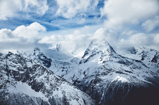 Panorama dramático de altas montanhas nevadas abaixo do céu nublado no inverno. Imagem da natureza selvagem