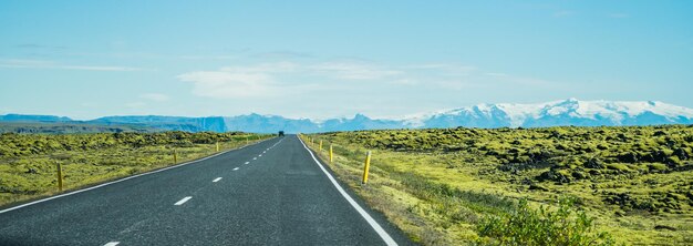 Panorâmica de uma longa estrada de asfalto cercada por campos gramados na Islândia