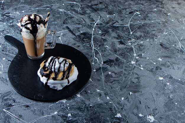 Panquecas com cobertura de chocolate e copo de café na placa de madeira.