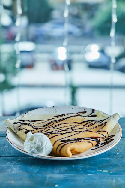 Panquecas com sorvete de baunilha, chocolate no prato branco na superfície azul