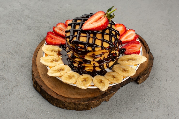 Foto grátis panquecas de vista superior gostoso delicioso com morangos vermelhos fatiados e bananas dentro de chapa branca sobre o fundo cinza