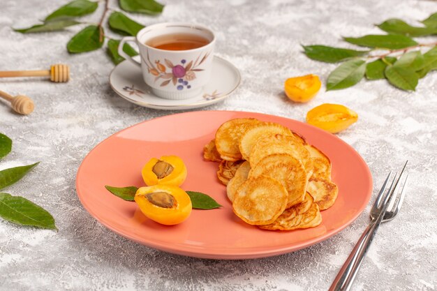 Panquecas doces de frente para o prato de pêssego com damascos e chá na mesa cinza. Panqueca comida refeição doce sobremesa fruta