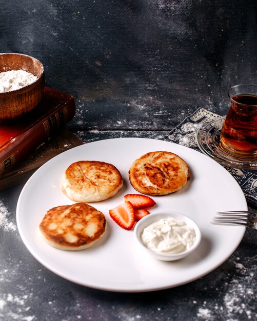 Panquecas saborosas de vista frontal, juntamente com chá quente com creme de leite e fatia de morango no backgorund brilhante