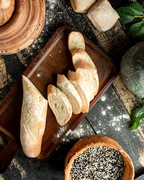 Pão baguete a bordo com gergelim e pães na mesa