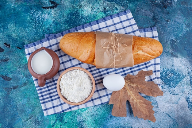 Pão baguete, farinha, ovo e leite na toalha de chá em azul.