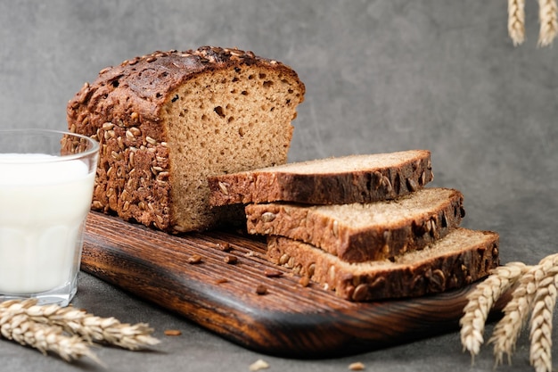 Pão caseiro de centeio com sementes cortadas em fatias encontra-se em uma tábua de corte. Pão de pão e copo de leite ideia de café da manhã saudável, foco seletivo, close-up. Espigas de trigo na mesa