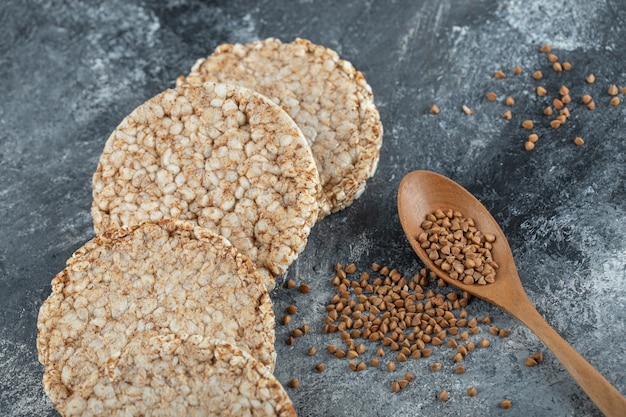 Pão crocante estufado e colher de pau de trigo sarraceno cru na superfície de mármore