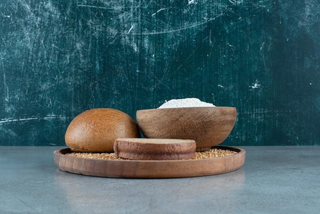 Pão de centeio com tigela de farinha na placa de madeira.