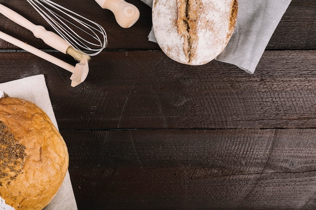 Pão de forma em papel de tecido com equipamentos de cozinha no fundo escuro de madeira