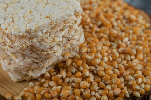 Pão estaladiço e sementes de milho cru em um pedaço de madeira